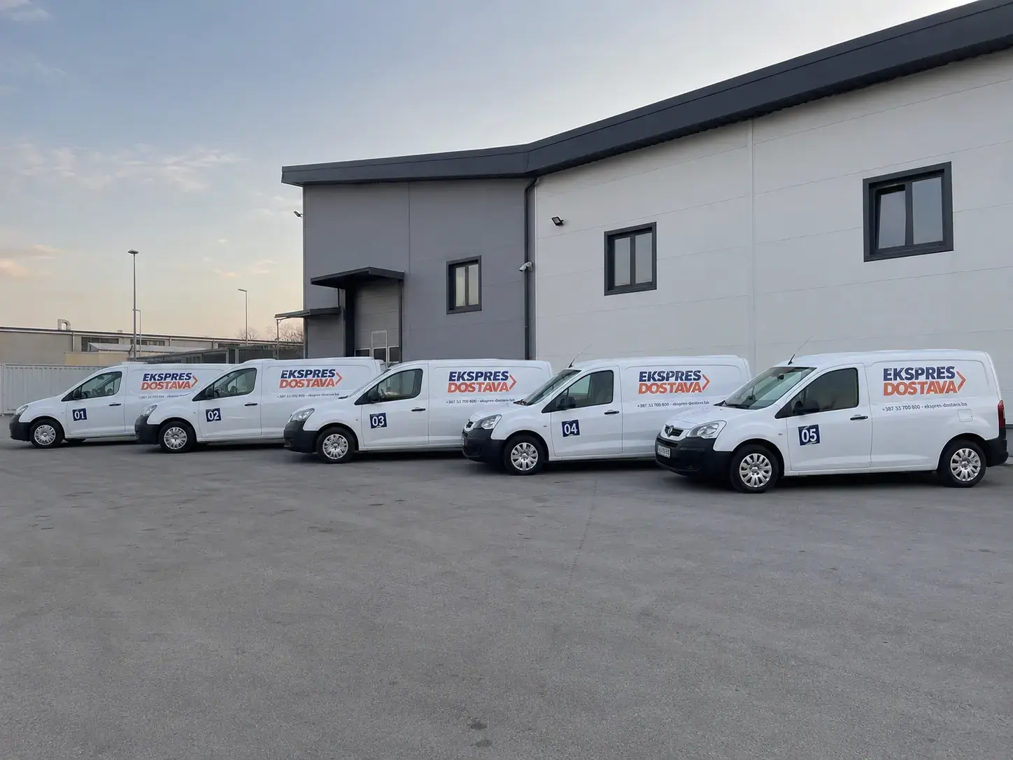 Pet brendiranih dostavnih kombija u nizu u logistički dvorište